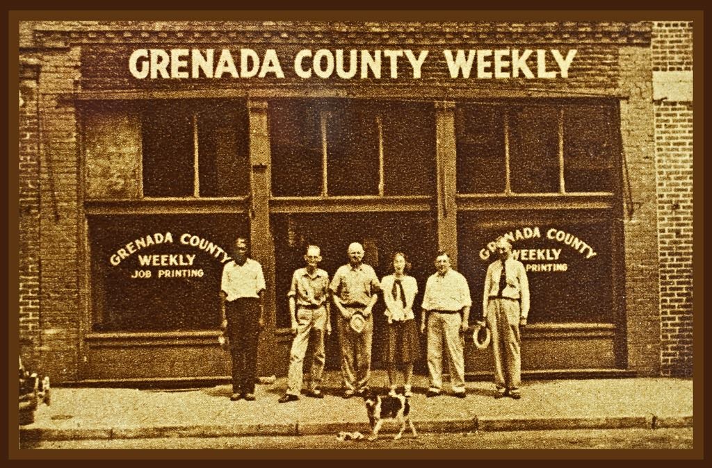 Antique photo of people standing on the sidewalk in front of the Grenada County Weekly building in downtown Grenada, MS.